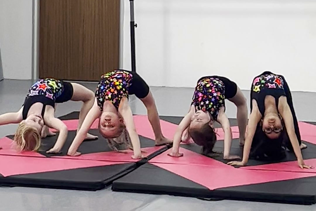 Four Kay Academy Acro students holding bridge positions on mats