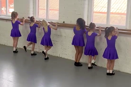 Young tap dancers practising at the barre with raised tap shoes